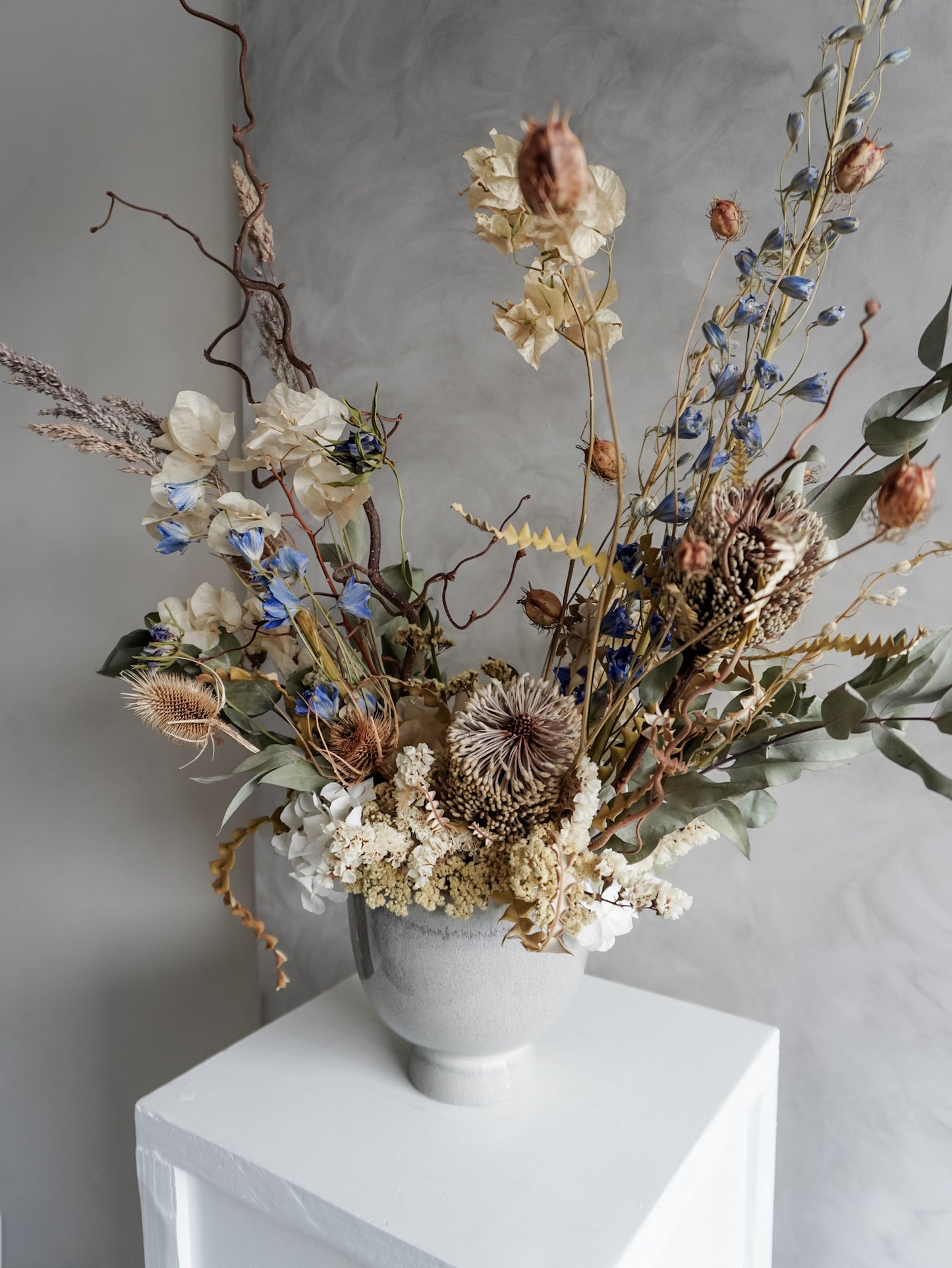 Neutral dried floral arrangement in a white vase against a gray textured wall.