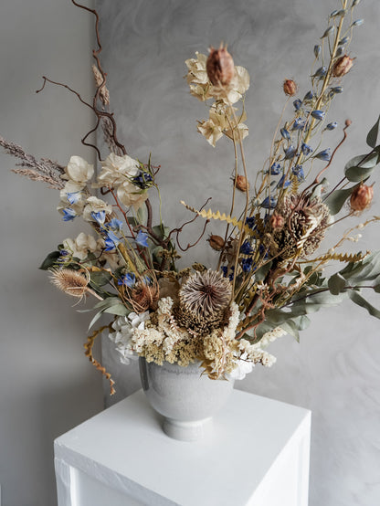 Neutral dried floral arrangement in a white vase against a gray textured wall.