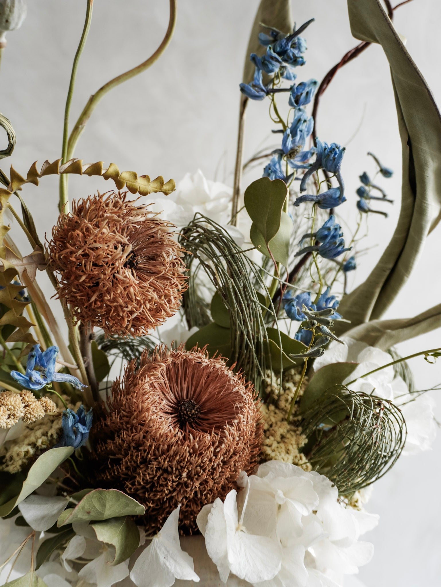 Dried flower arrangement in natural green and white tones in a white ceramic vase - close up view.