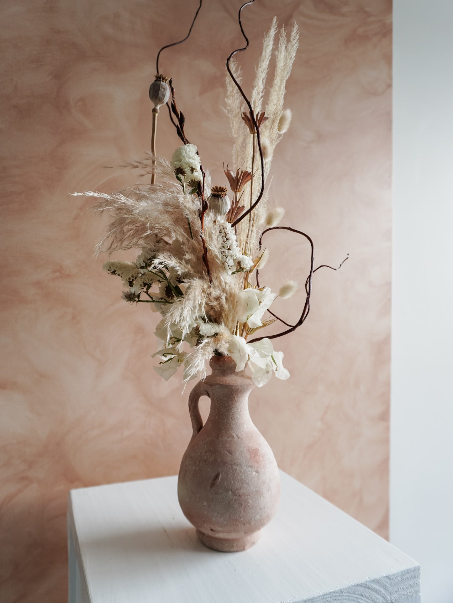 Terracotta vase with dried flowers against a soft pink background.