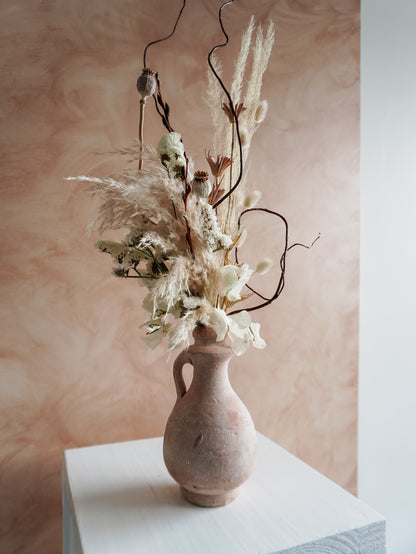 Terracotta vase with dried flowers against a soft pink background.