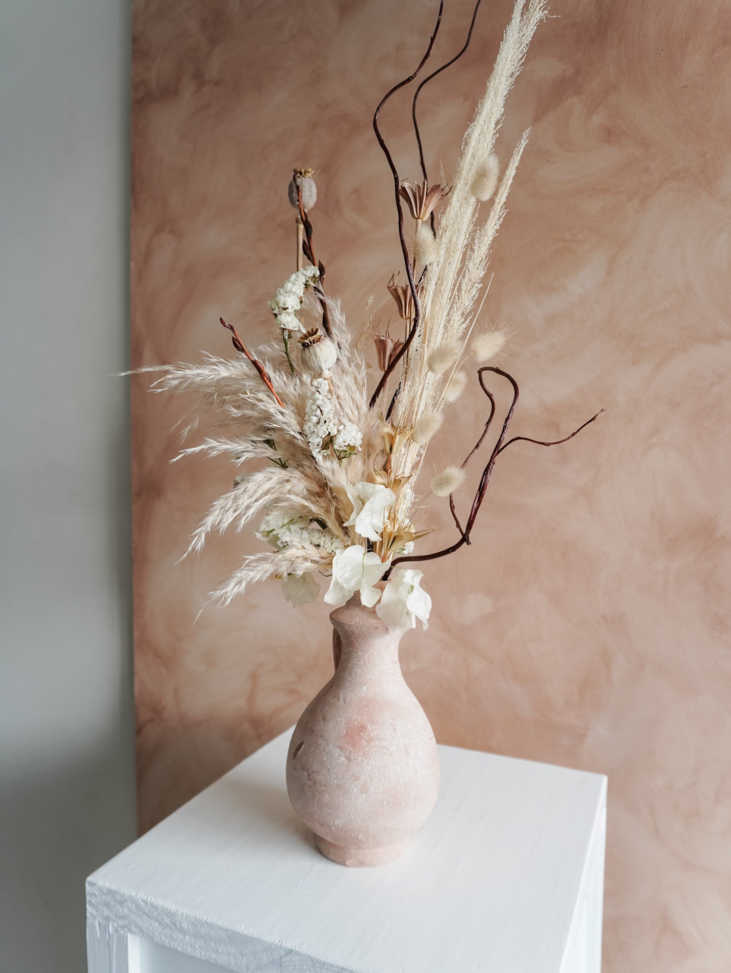Terracotta vase with dried flowers against a soft pink background.