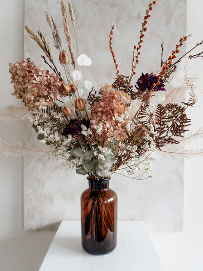 Dried flower arrangement in amber bottle with pastel florals – close view.