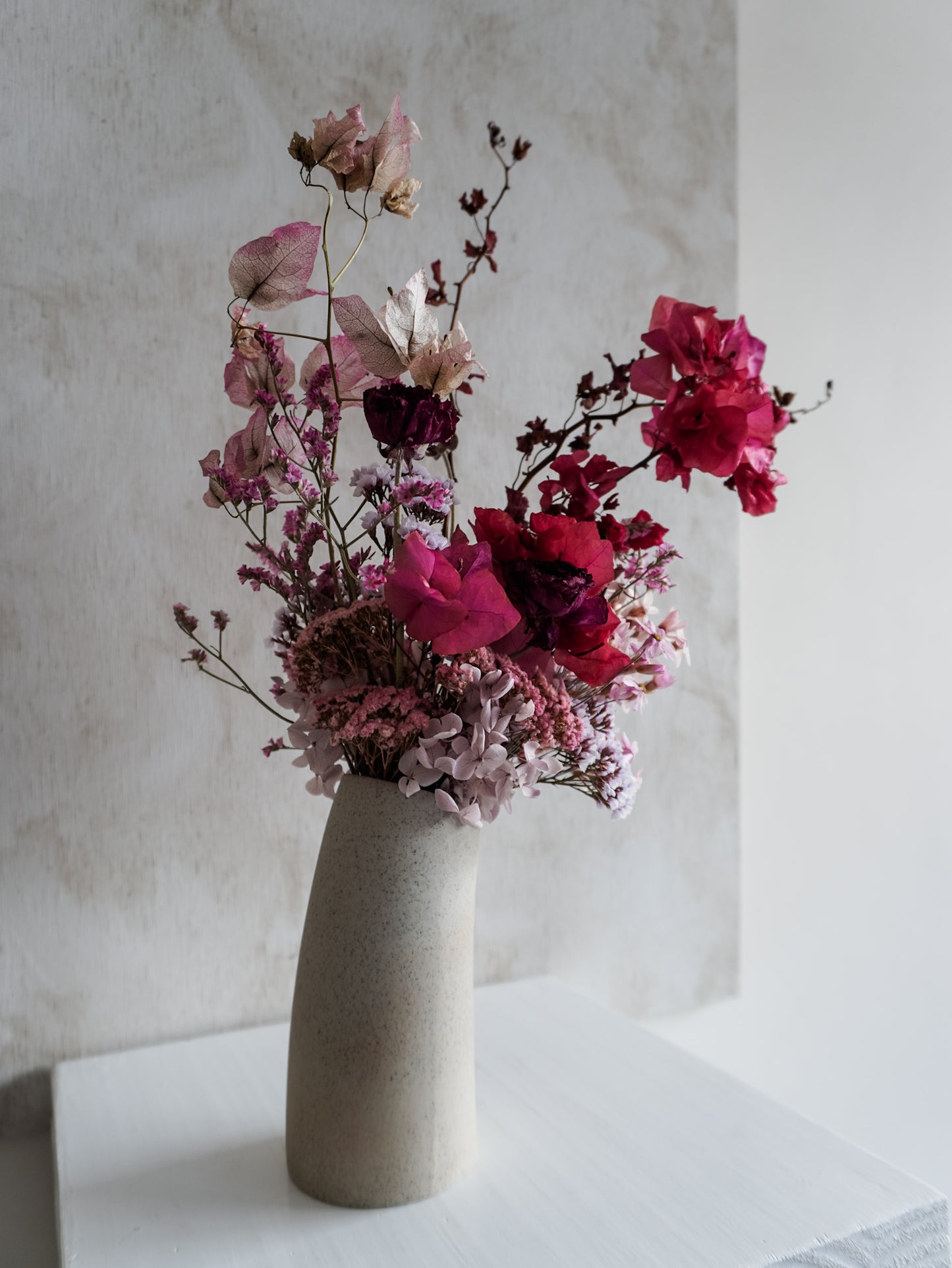 Dried flower arrangement in ceramic vase with deep pink florals – left side view.