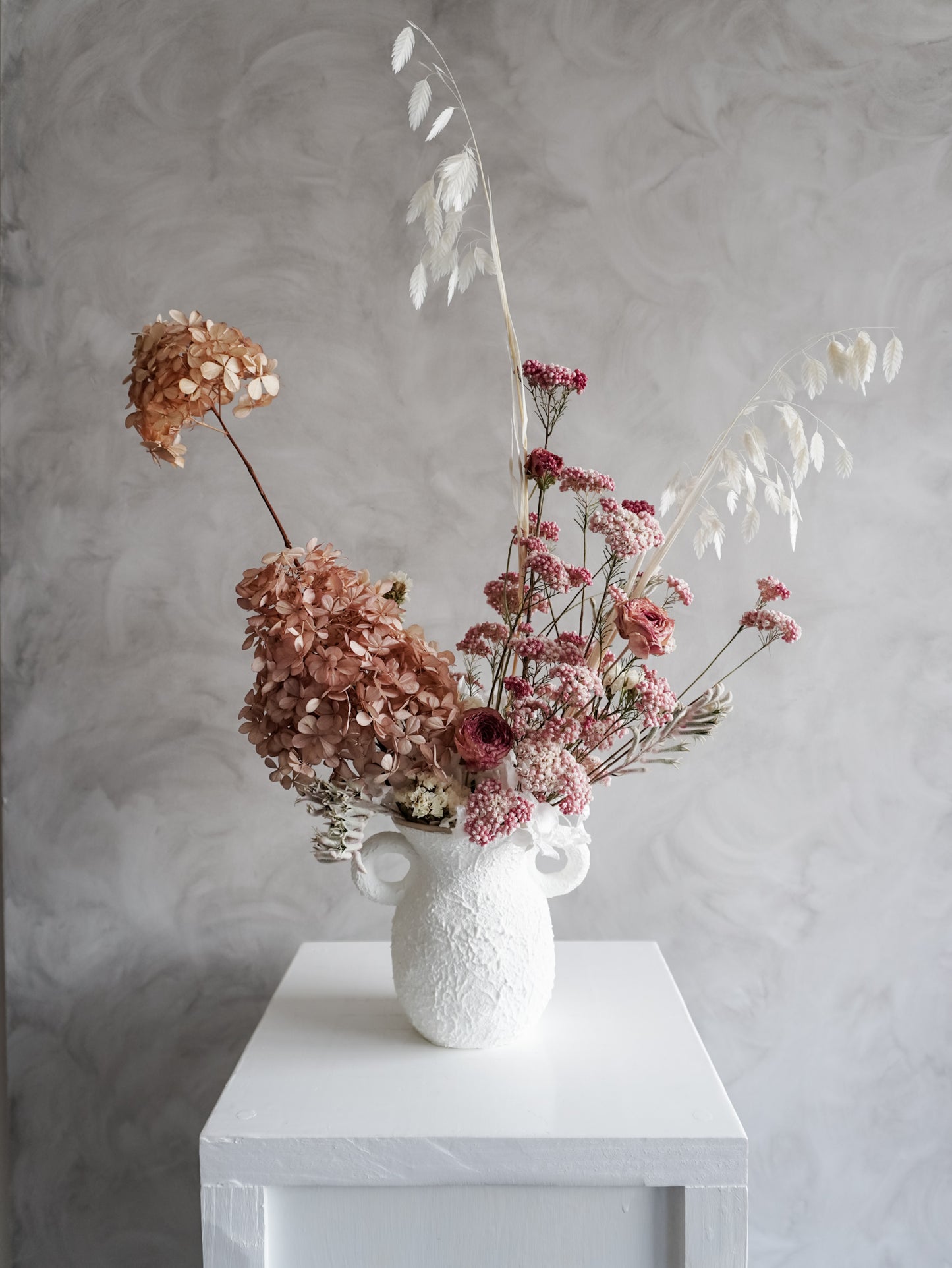 Dried flower arrangement in ceramic urn vase with soft pink florals – distant view.