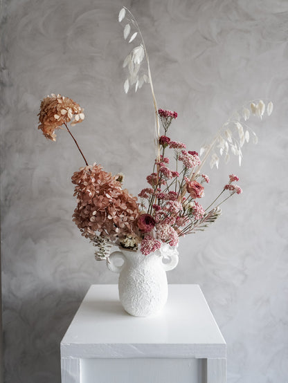 Dried flower arrangement in ceramic urn vase with soft pink florals – distant view.