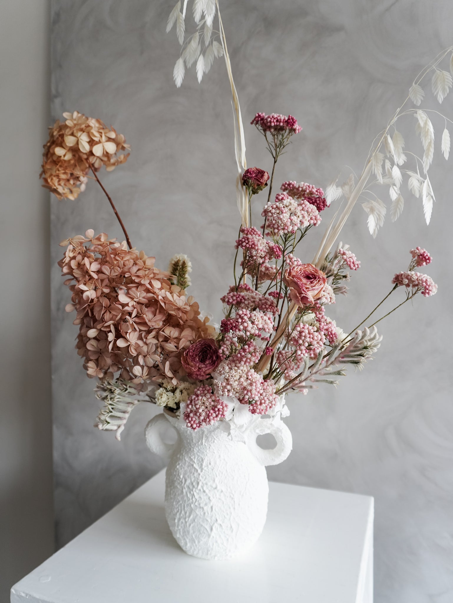White textured vase with dried flowers against a gray background