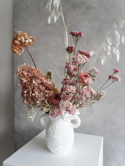 White textured vase with dried flowers against a gray background
