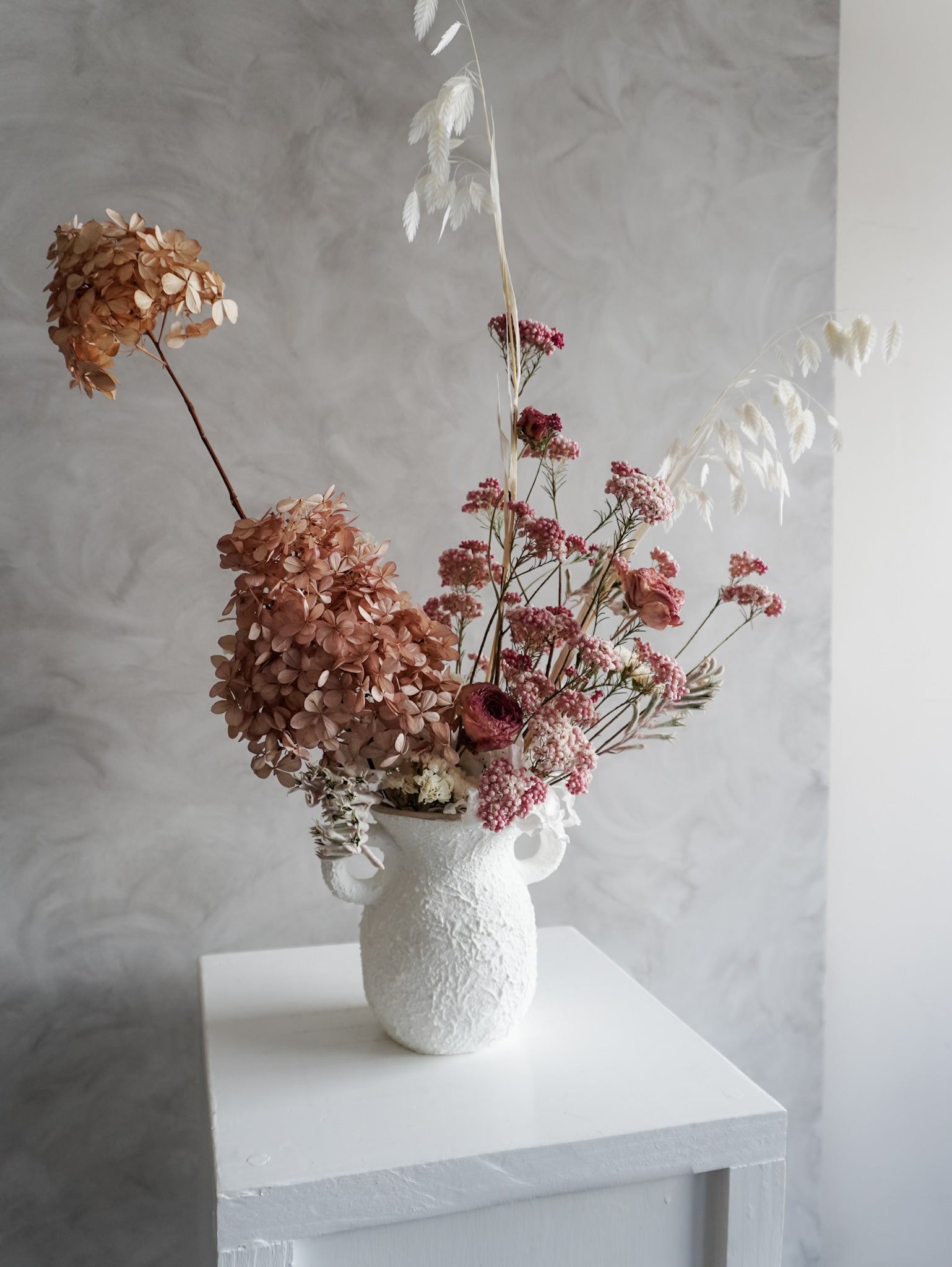 White textured vase with dried flowers on a white surface against a light gray wall
