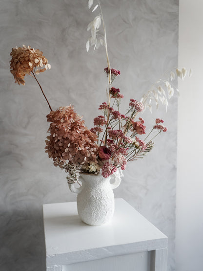White textured vase with dried flowers on a white surface against a light gray wall