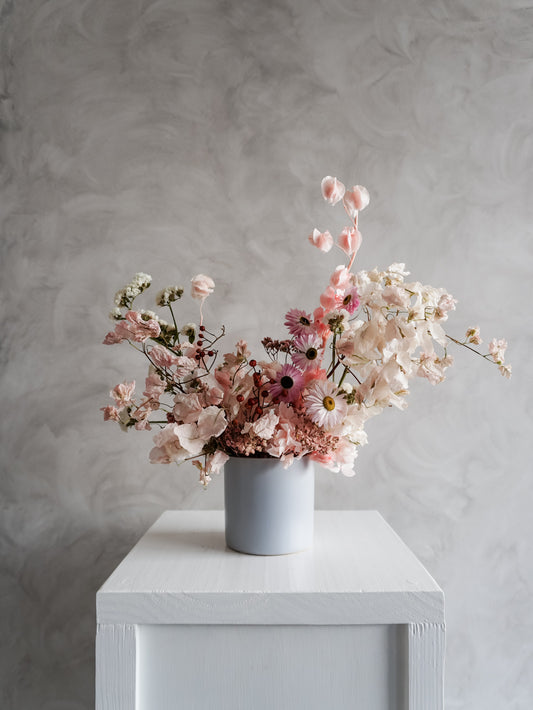 Dried flower arrangement in soft blue ceramic vessel with textural pastel florals – distant view.