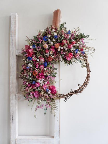 Dried flower wreath in bright, colourful tones with spring florals on a grapevine base – distant view.