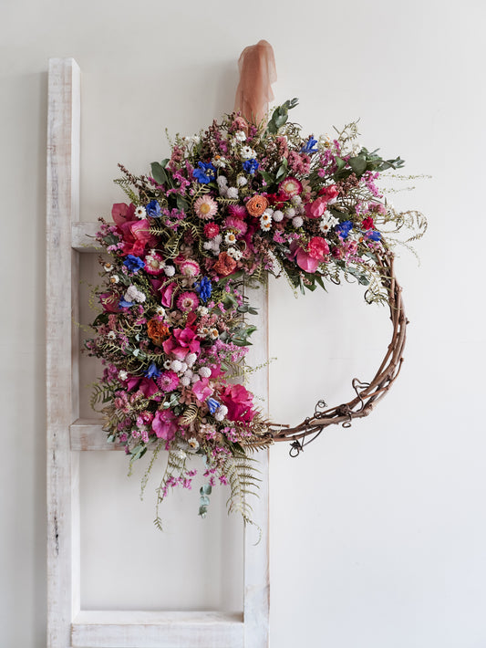 Dried flower wreath in bright, colourful tones with spring florals on a grapevine base – distant view.