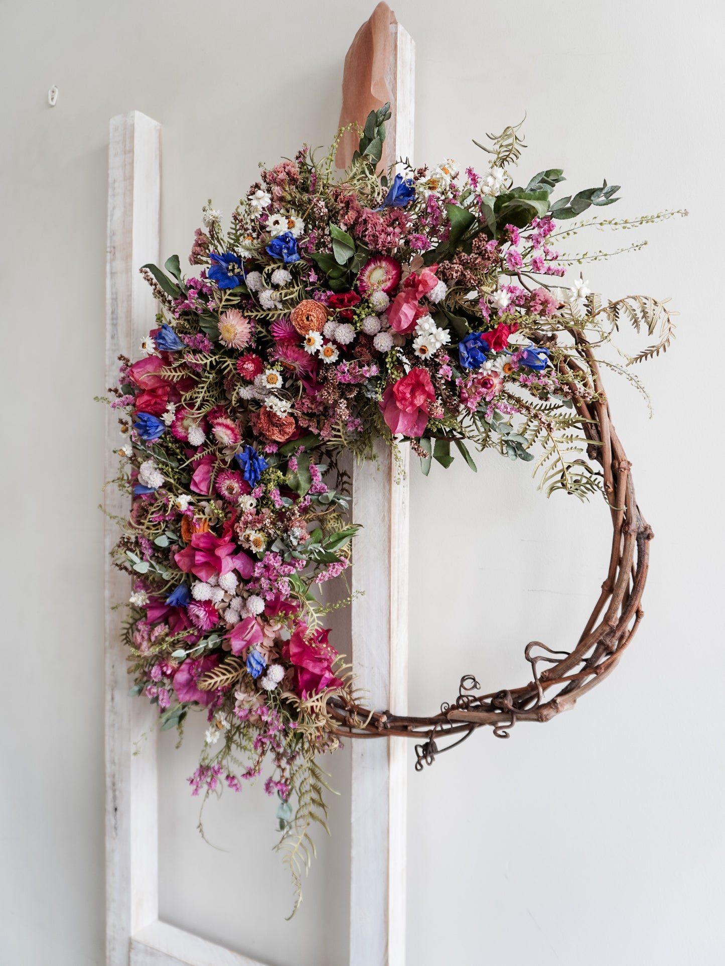 Dried flower wreath in bright, colourful tones with spring florals on a grapevine base – side view.