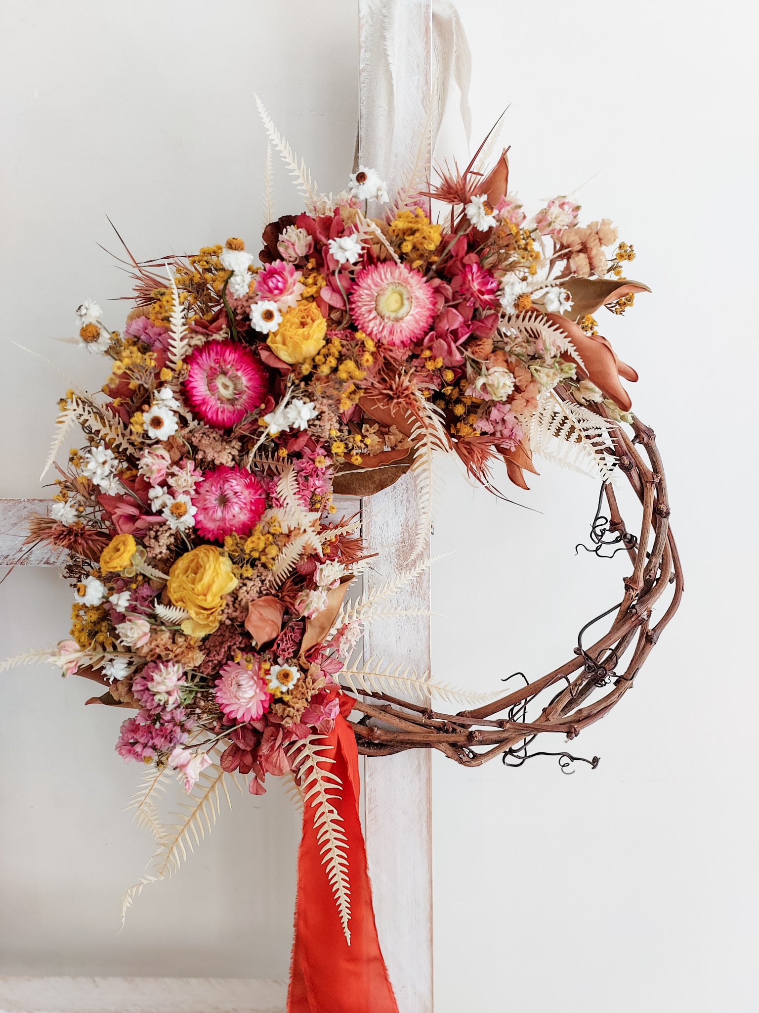 Dried flower wreath in bright pinks and yellows on a grapevine base.
