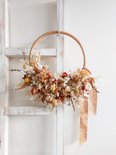 Load image into Gallery viewer, Dried flower wreath in warm tones on a rattan hoop base – distant full view.
