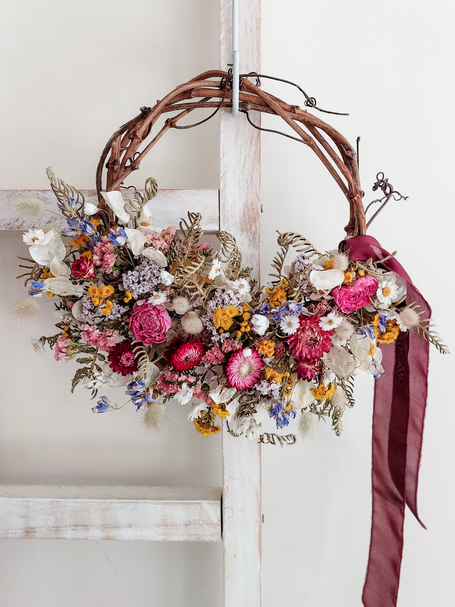 Dried flower wreath in bright colourful tones on a grapevine base.