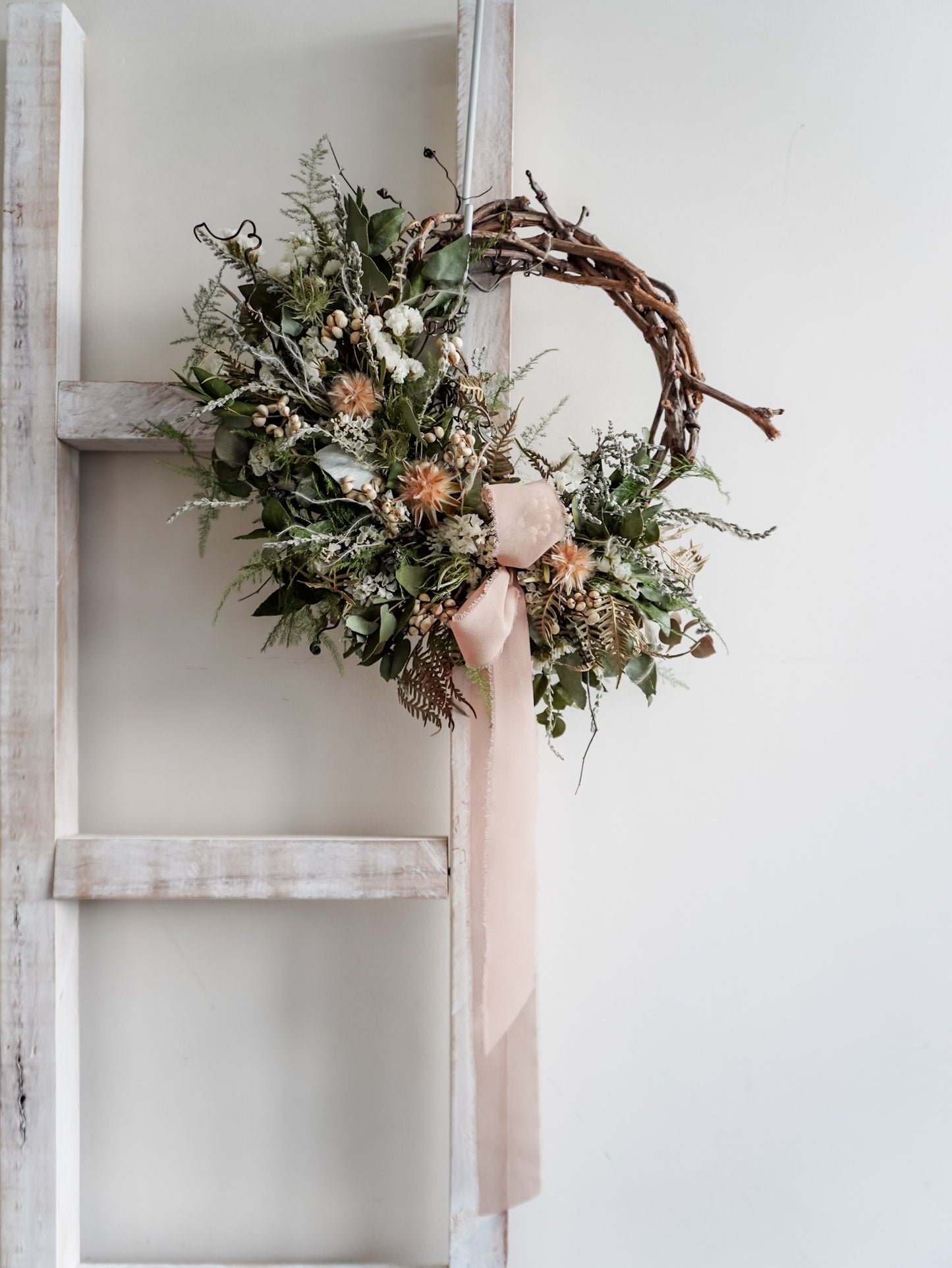 Dried flower wreath in natural Christmas inspired tones on a grapevine base – distant view.