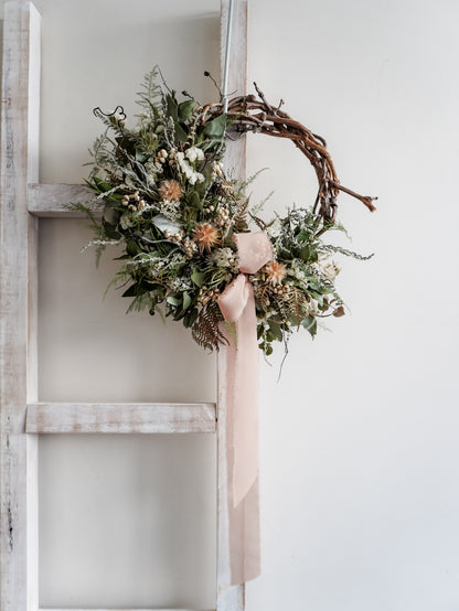 Dried flower wreath in natural Christmas inspired tones on a grapevine base – distant view.