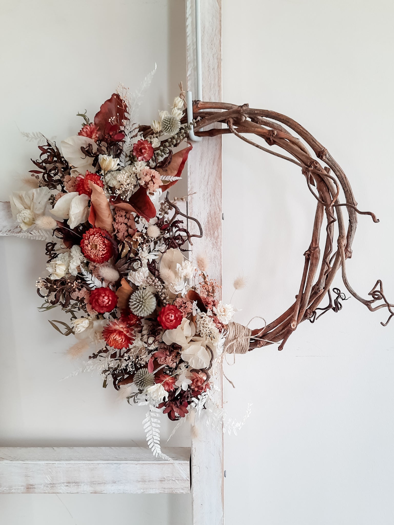Dried flower wreath in rich reds and neutrals on a grapevine base.