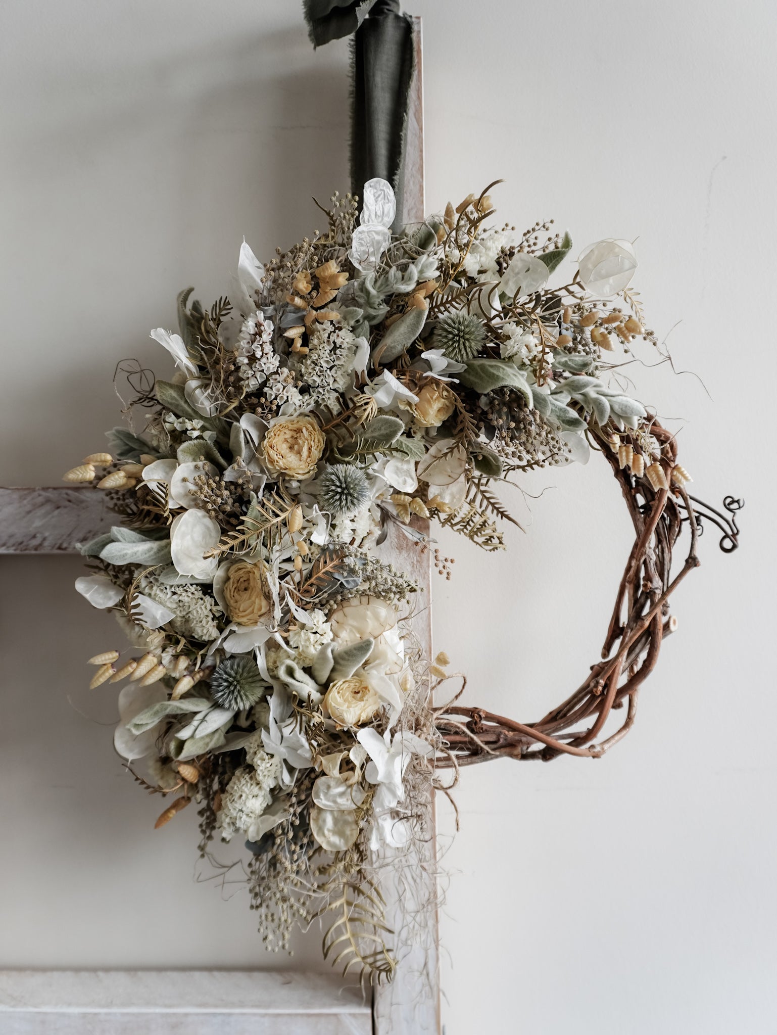 Decorative wreath with dried flowers and leaves on a white wall.