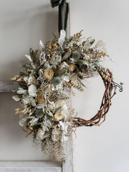 Decorative wreath with dried flowers and leaves on a white wall.