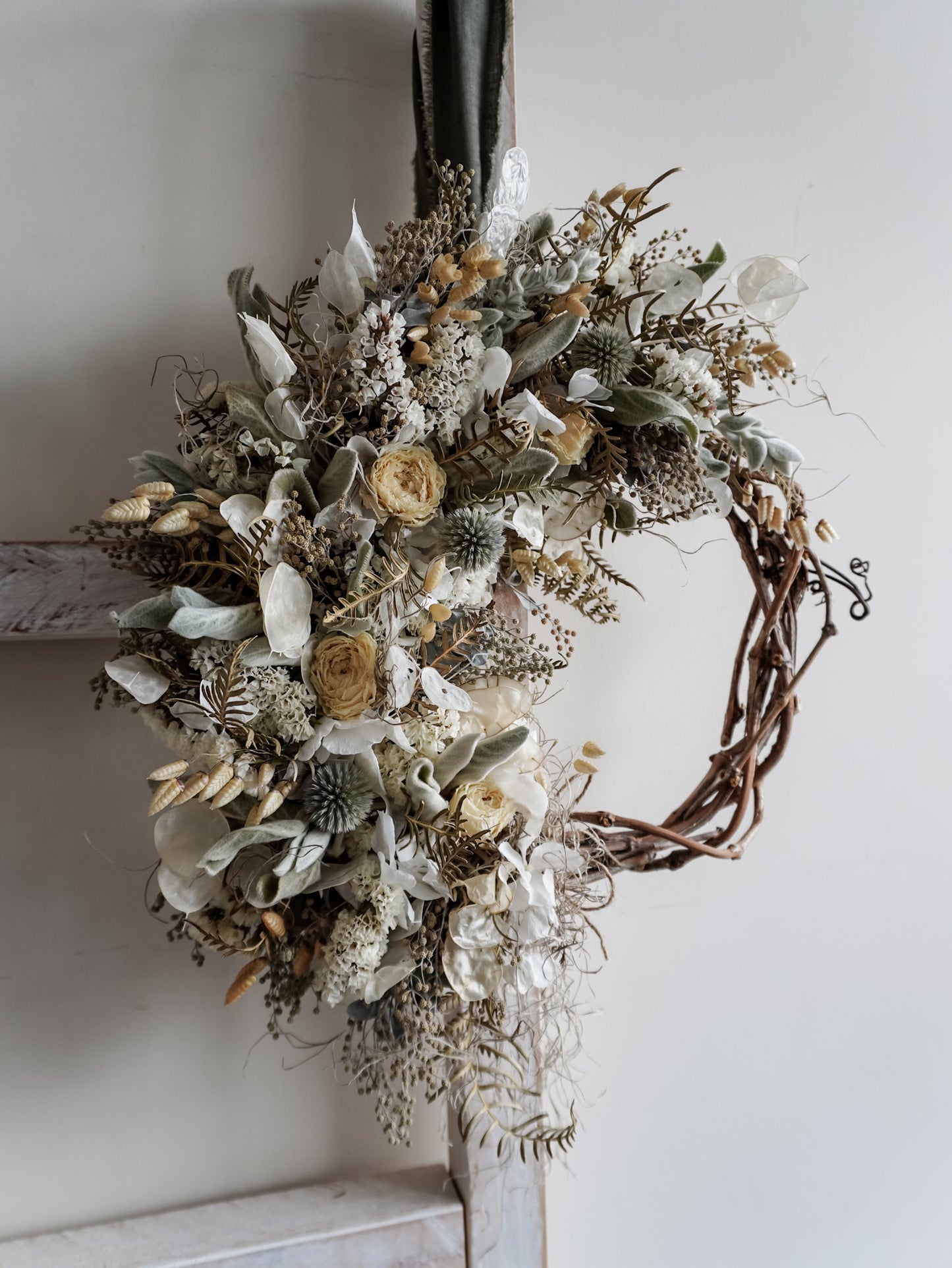 Decorative wreath with dried flowers and leaves on a white wall.