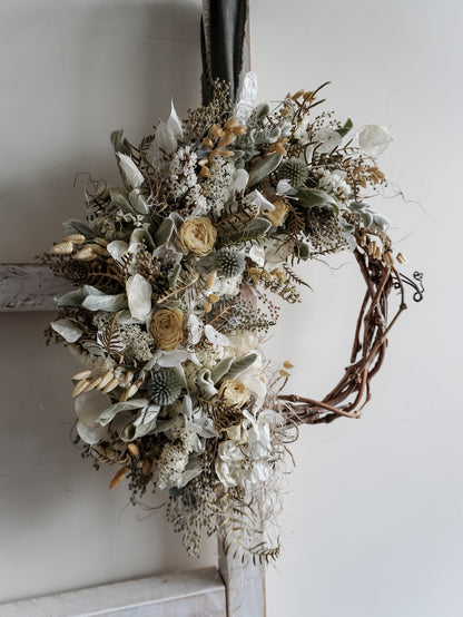 Decorative wreath with dried flowers and leaves on a white wall.