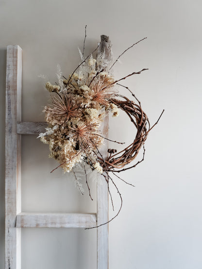 Dried flower wreath in nude neutral tones spray design on a grapevine base – distant view.