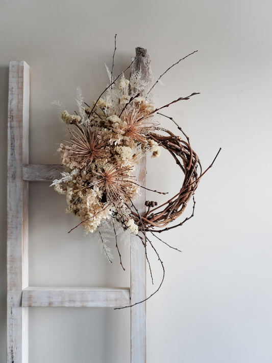 Dried flower wreath in nude neutral tones spray design on a grapevine base – distant view.