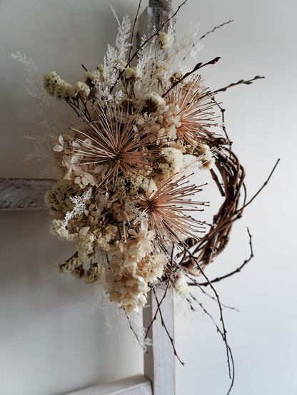 Dried flower wreath in nude neutral tones spray design on a grapevine base – side full view.