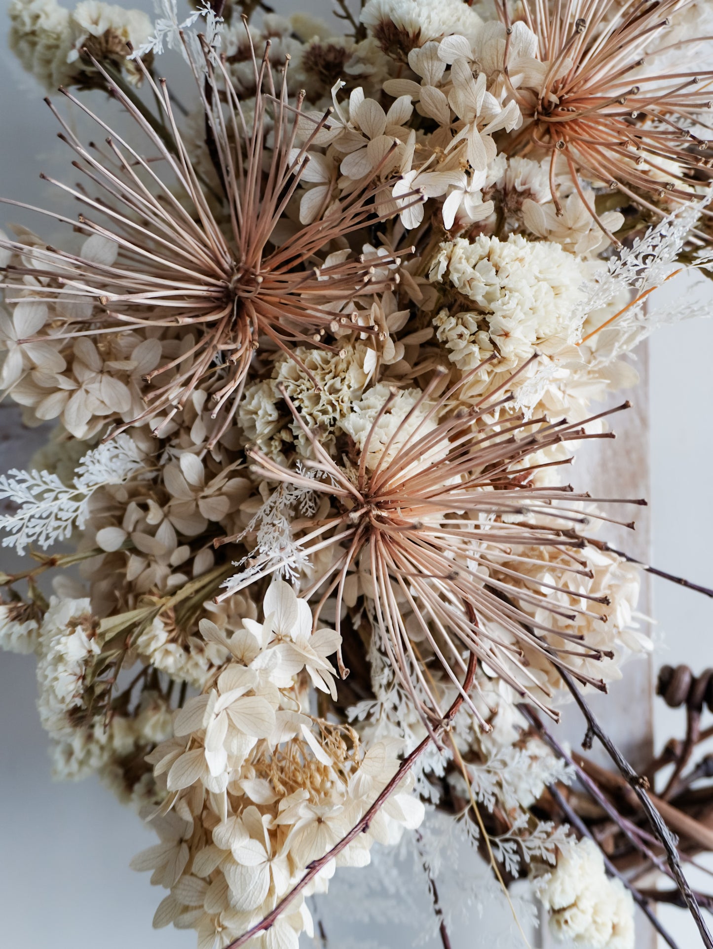 Dried flower wreath in nude neutral tones spray design on a grapevine base – close up view of agapanthus.