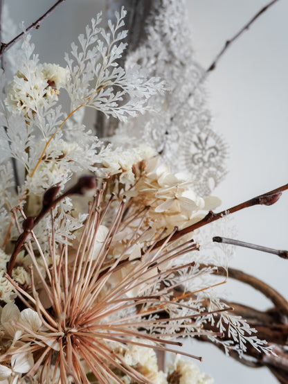 Dried flower wreath in nude neutral tones spray design on a grapevine base – close up of fern and lace.