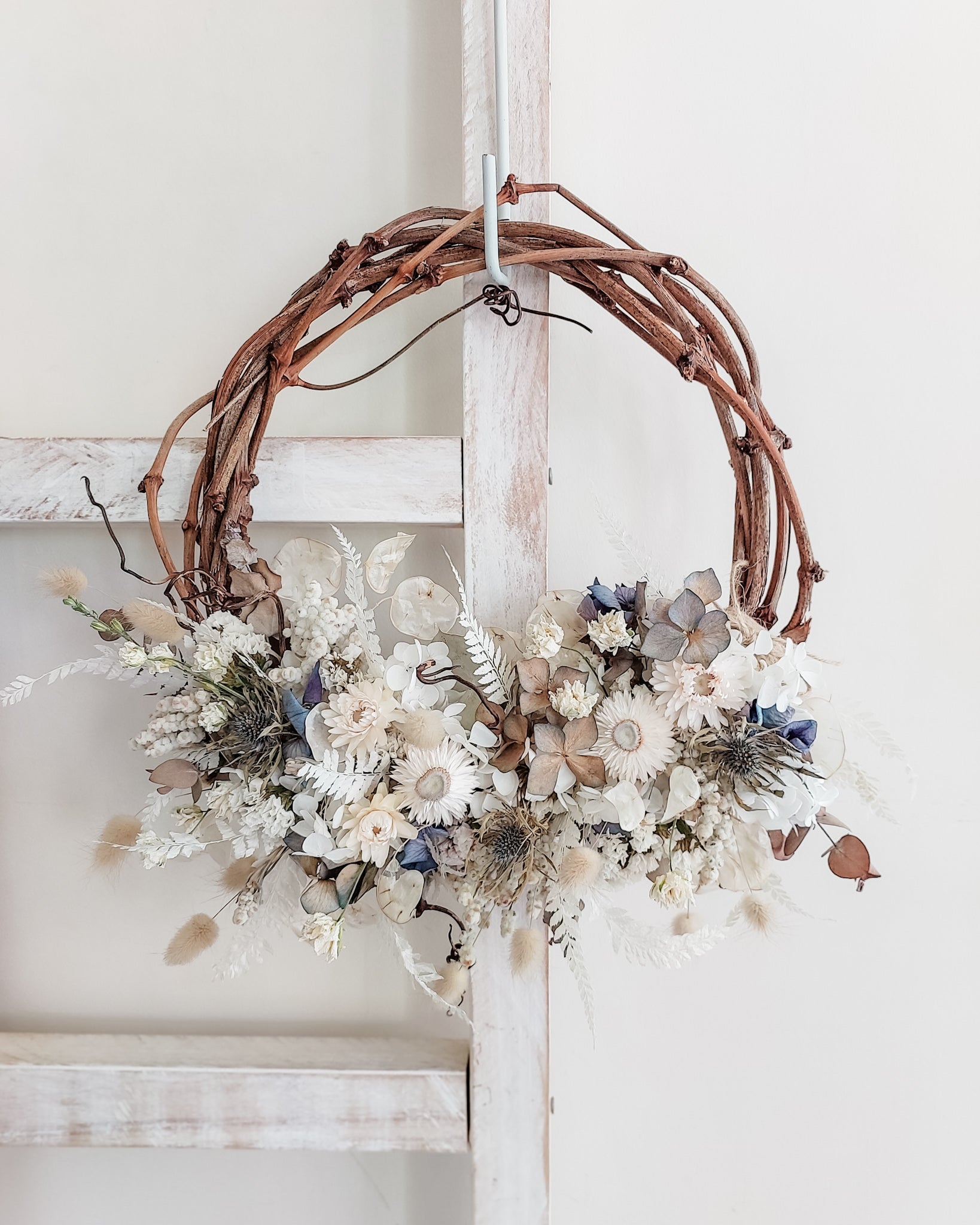Dried flower wreath in soft blue and neutral tones on a grapevine base.