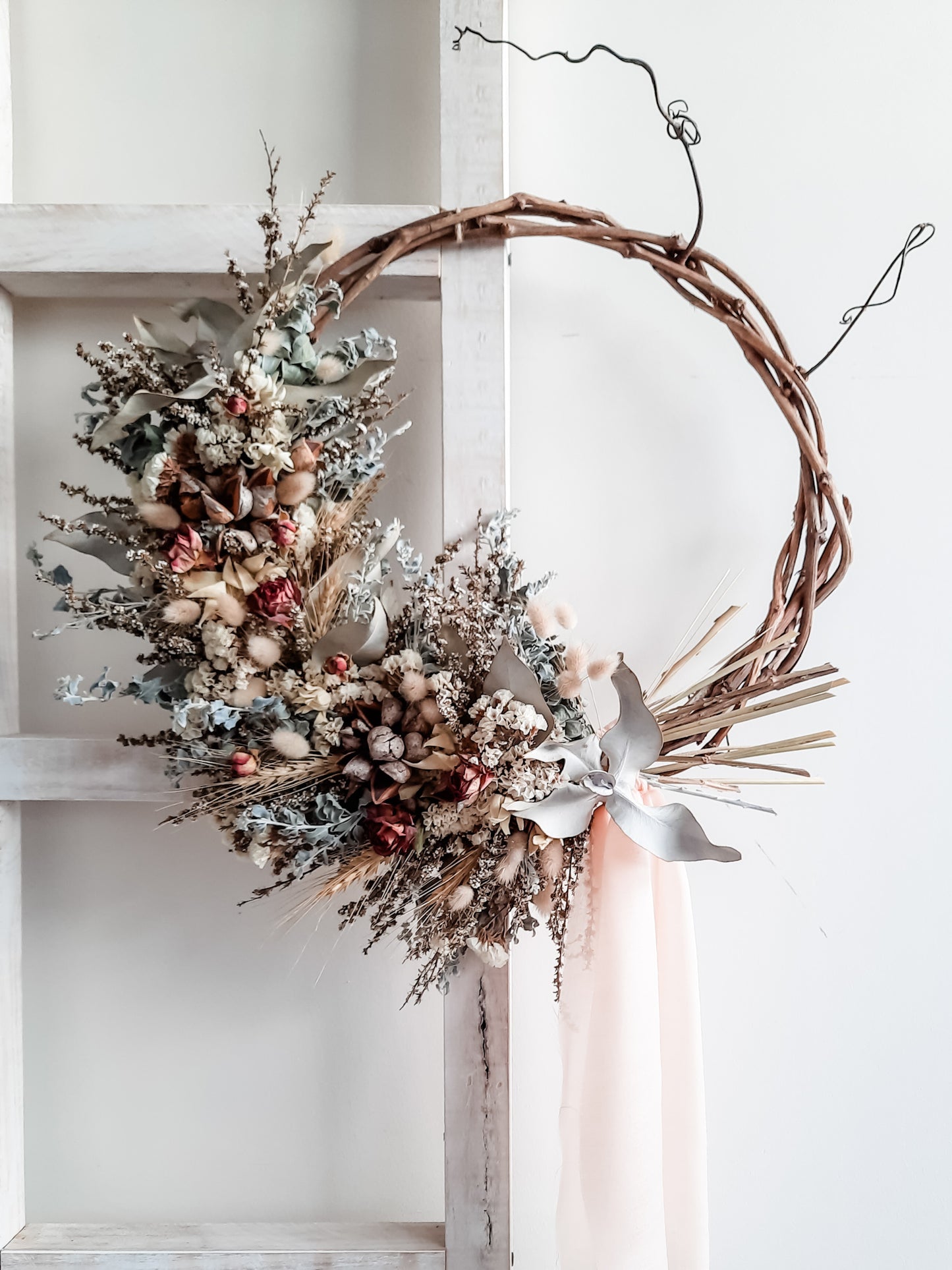 Dried flower wreath in soft pastel tones on a grapevine base.