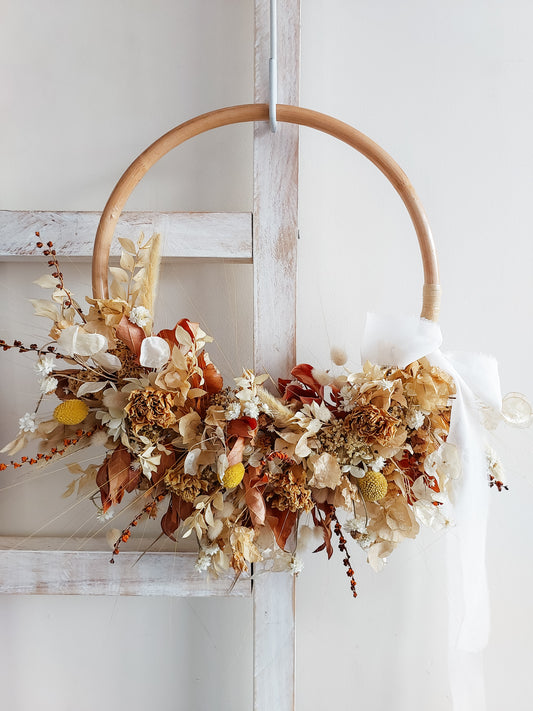 Dried flower wreath in warm tones on a rattan hoop base – close full view.