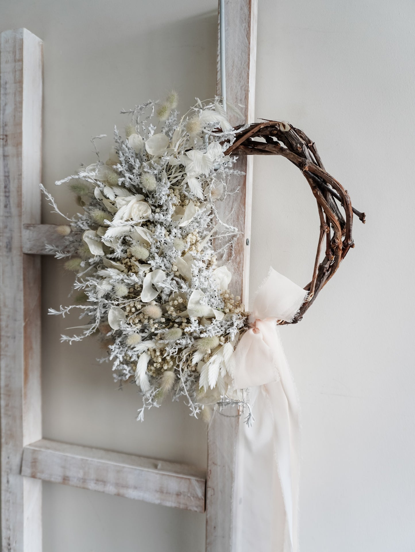 Dried flower wreath in classic white Christmas inspired tones on a grapevine base – close side view.