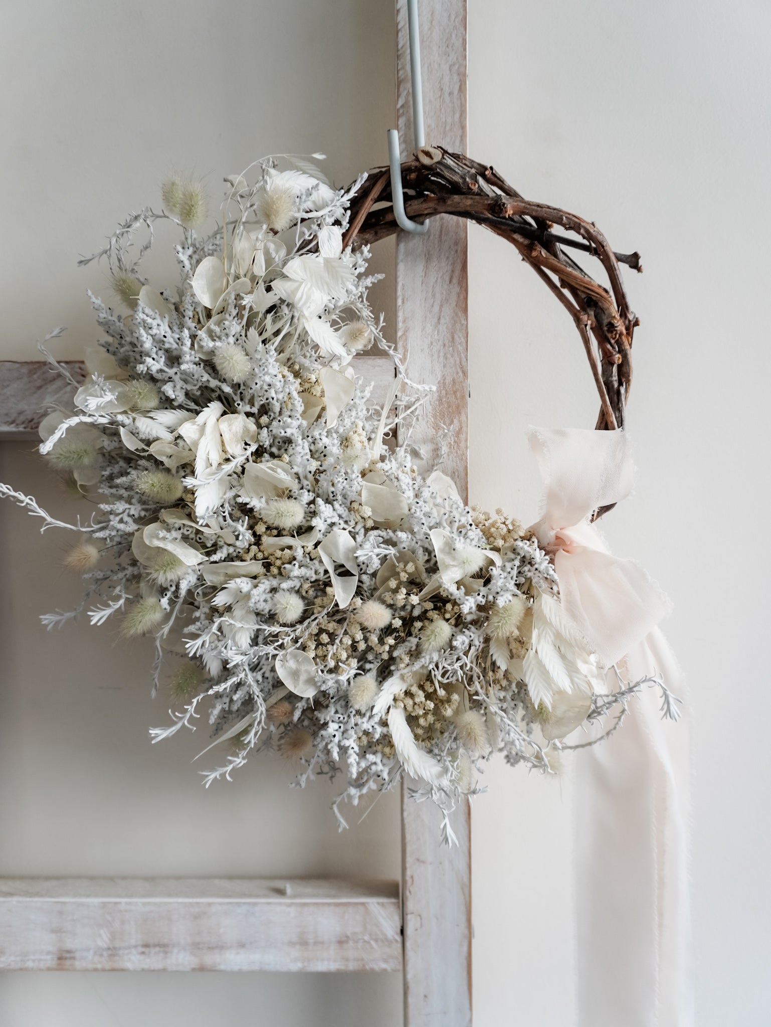 Dried flower wreath in classic white Christmas inspired tones on a grapevine base – close full view with angle variation.