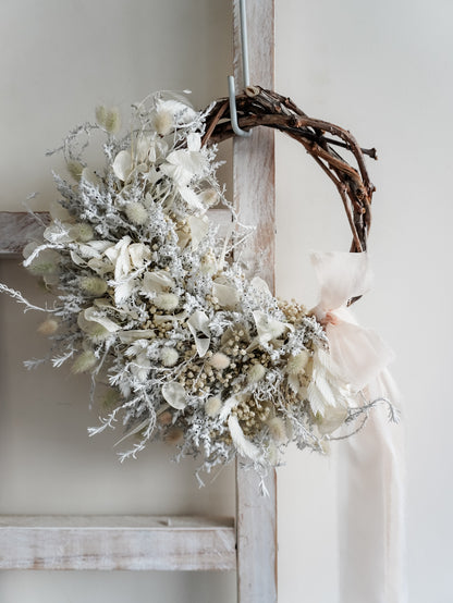 Dried flower wreath in classic white Christmas inspired tones on a grapevine base – close full view with angle variation.